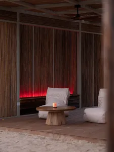 Cozy indoor living area with a wooden deck, two chairs, two couches, and a dining table in the background, featuring warm wood tones and comfortable seating options