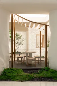 A modern dining area with a wooden table, glass top, and comfortable seating, surrounded by potted plants and a well-designed atmosphere