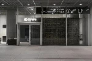 Modern shopping center exterior with a large glass wall, black tile accents, and a bench in front