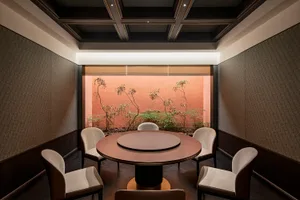A modern dining space with a round wooden table, three chairs, and red brick and white painted walls creating a cozy atmosphere