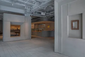 Empty restaurant interior with concrete walls, high ceilings, and scattered chairs, conveying a clean and functional atmosphere