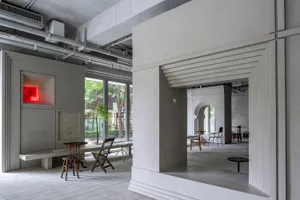 A modern industrial lobby with concrete walls, featuring chairs and dining tables, and a minimalist atmosphere