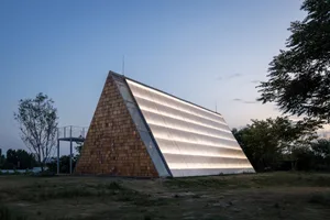 A modern building with a triangular shape, featuring a wood and glass design, with a brightly lit interior and ample windows allowing natural light to enter