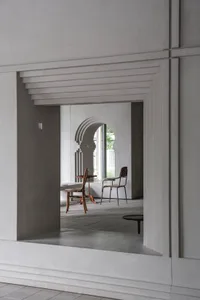 Empty living area with a white wall, a doorway, two chairs, and a table, creating a calm and minimalistic atmosphere