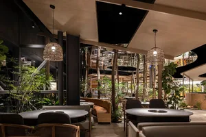 A modern restaurant with dining tables, chairs, and potted plants, creating a warm and inviting atmosphere