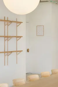 A clean and organized interior space with a white wall and three wooden shelves of varying heights, creating a minimalist atmosphere