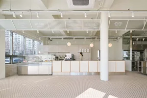 A modern kitchen with white walls, a tile floor, and appliances, including two ovens and three refrigerators, with natural light coming through windows