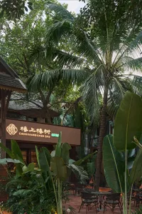 A tropical restaurant with a brown exterior, a palm tree in front, and lush surroundings with potted plants
