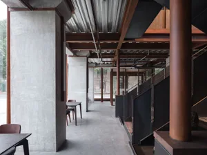 A modern building with concrete walls and floors, featuring multiple rooms, staircases, and chairs, conveying a sense of spaciousness and functionality