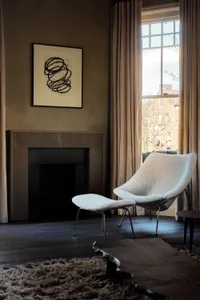 Cozy living space with a white chair in front of a fireplace, two windows on either side, and natural light from the windows