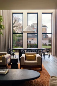 Open living area with a large window, chairs, dining table, and a couch, surrounded by natural light