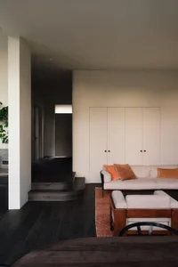 Cozy living room with hardwood floors, white walls, a couch, two chairs, and a potted plant adding greenery to the space