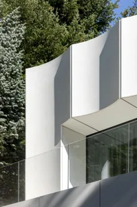 A modern building with a large glass wall and a concrete exterior, surrounded by trees