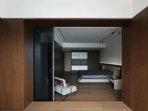 Cozy bedroom with wooden floors and walls, featuring two beds and a chair, with a warm and inviting atmosphere