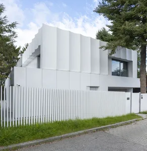 A modern house with a concrete exterior, large windows, and a tree in front