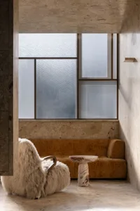 Cozy living area with a couch, chair, and table, surrounded by stone walls and natural light from two windows
