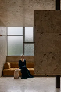 A woman sits on a couch in a living area with a large window, vases, and a bowl, surrounded by a comfortable and inviting atmosphere