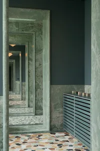 Large bathroom with multiple mirrors, green marble floors, and a heater, creating a modern and sophisticated space with a focus on functionality and aesthetics