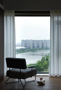 A modern living area with a black chair and couch, offering a panoramic city view through a large window