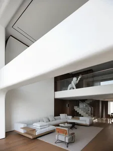 Open modern living area with a white couch, a sculpture on the wall, two chairs, a dining table, and a potted plant, creating a clean and inviting atmosphere