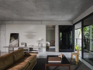 A modern living room with a large couch, chair, dining table, two beds, bookshelf, and clock, set against a clean and minimalist backdrop of white walls and grey flooring