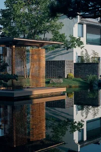 A large white house with a modern design, surrounded by trees and a pond, creating a serene atmosphere