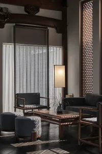 A modern living area with a couch, chair, coffee table, and lamp, surrounded by potted plants and a cozy atmosphere