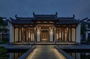 A stone building with intricate details and decorative elements, surrounded by a courtyard with lanterns and statues, conveying a sense of history and craftsmanship