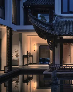 A serene Asian-style house with a large roof, wooden walls, and a courtyard featuring a pond, chairs, and a tranquil atmosphere