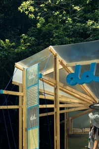 An open-air structure with a large wooden roof, a wooden frame, and clear plastic walls, featuring two people standing inside
