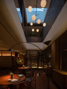 Warm and inviting dining space with multiple tables, chairs, potted plants, and hanging lights
