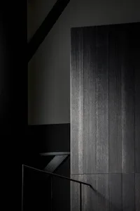 A modern interior space with a staircase made of wood, black walls, and a doorway leading to another level