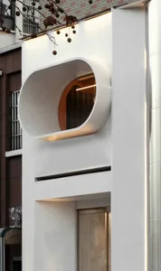A modern building facade with a large white concrete wall featuring a round window, set against a neutral background