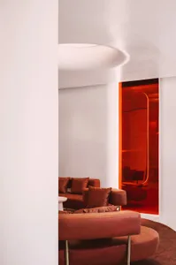 Cozy modern living area with brown leather couches and chairs in front of a red accent wall on a white background