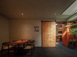 A warm and inviting restaurant dining area with wooden furniture, multiple dining tables, and a large wooden door leading to another room