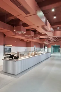 Modern restaurant kitchen with a counter, sink, cabinets, refrigerator, and ovens, featuring neutral tones and a clean atmosphere