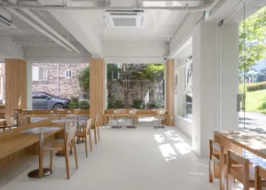 Empty restaurant interior with wooden floors, white walls, and a view of a car outside through a window