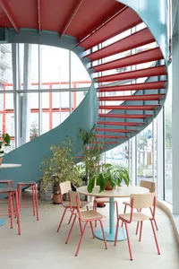 Inviting cafe interior with a spiral staircase, potted plants, and a dining table, surrounded by chairs and comfortable seating