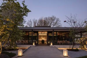 Modern restaurant with a black facade, multiple tables, chairs, and potted plants, emphasizing functionality and comfort