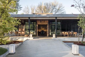 Modern restaurant with glass walls, wood accents, and natural light, featuring dining tables and chairs in a comfortable and inviting atmosphere