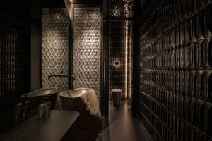 Bathroom with two sinks, a toilet, and black tile walls and floor, giving a clean and organized appearance