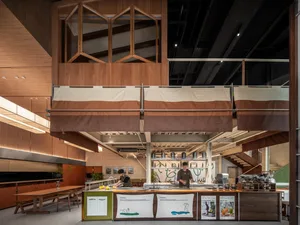 Casual restaurant kitchen with wooden floors and walls, featuring a counter with food preparation and potted plants, creating a welcoming atmosphere