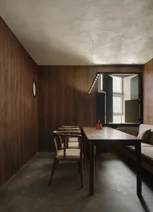 Cozy living area with a dining table, couch, and wooden walls, featuring a modern design and a clock on the wall