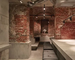 A large interior space with stone walls, brick floors, and several benches, giving off a vintage feel