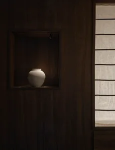 A dimly lit bathroom with a wooden cabinet featuring a white vase, creating a calm and serene atmosphere