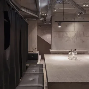 Modern bar space with a concrete countertop, stone wall, and black leather chairs, featuring bottles on display