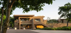 A brown building with a yellow accent and a large staircase leading to a second floor, surrounded by chairs in a gathering or event space