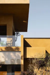 A residential house with a yellow exterior, a large window, and two chairs in front, showcasing a warm and inviting atmosphere