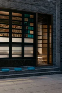 A modern building interior with a large window and glass door, featuring three blue stools outside the entrance, allowing natural light to enter the space