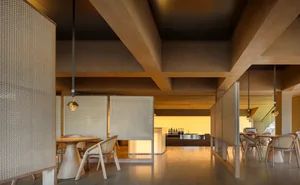 Open living area with wooden floors and walls, featuring a dining table, chairs, refrigerator, sink, and microwave, with a modern and contemporary design